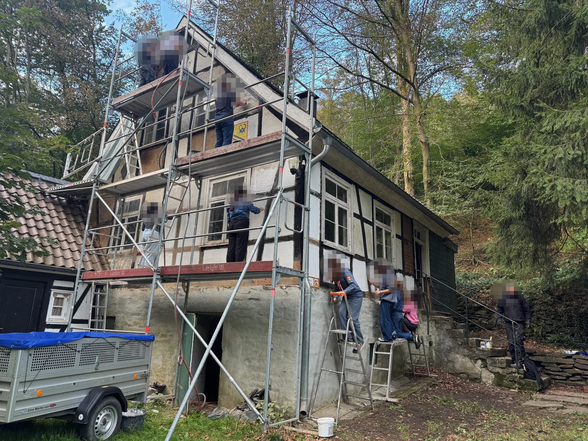 Eine große Gruppe streicht vom Gerüst und von Leitern aus die Gefache der Fassade weiß.