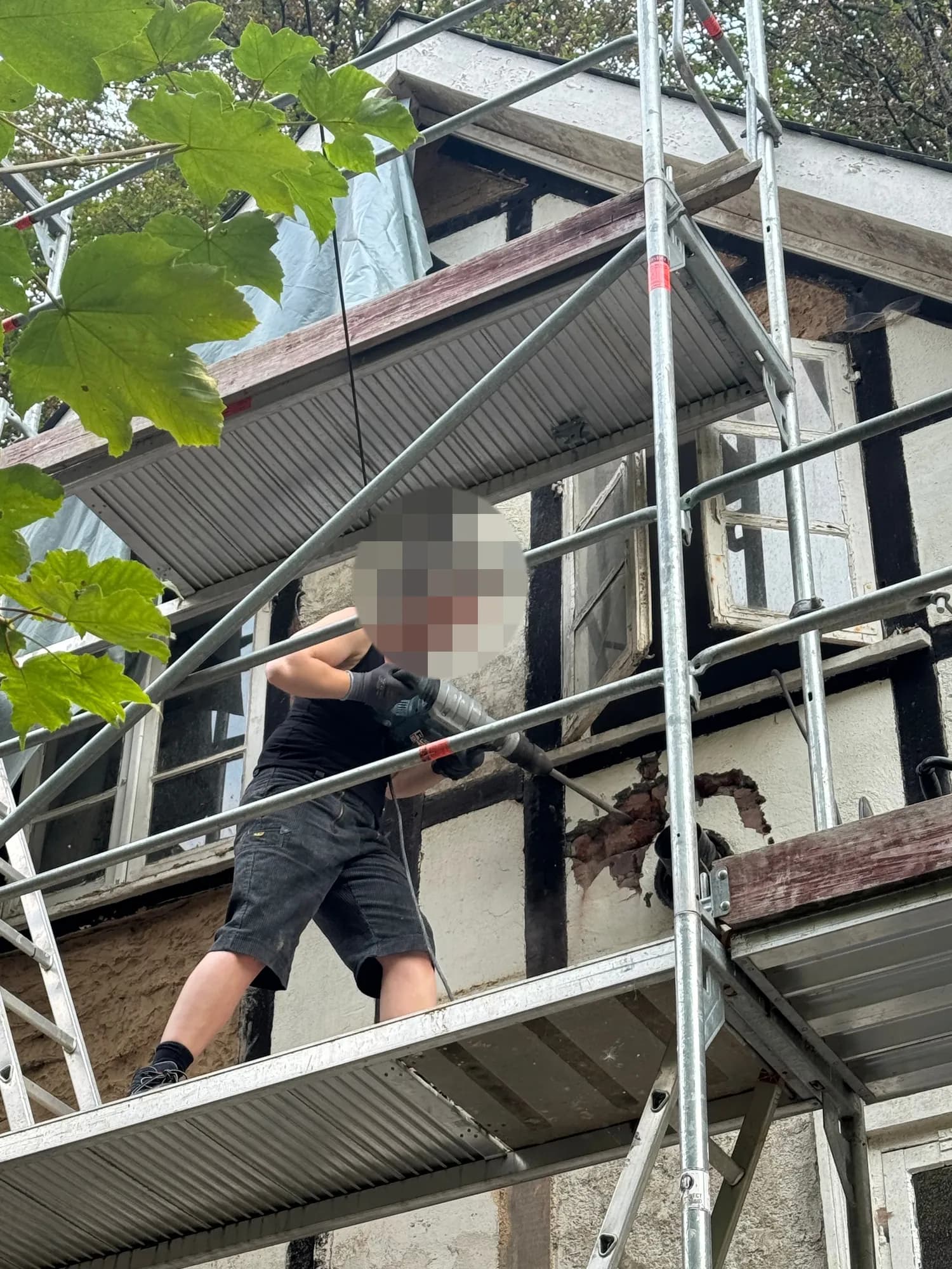Eine Person auf dem Gerüst stemmt mit einem Abbruchhammer Putz und Füllung aus einem Gefach.