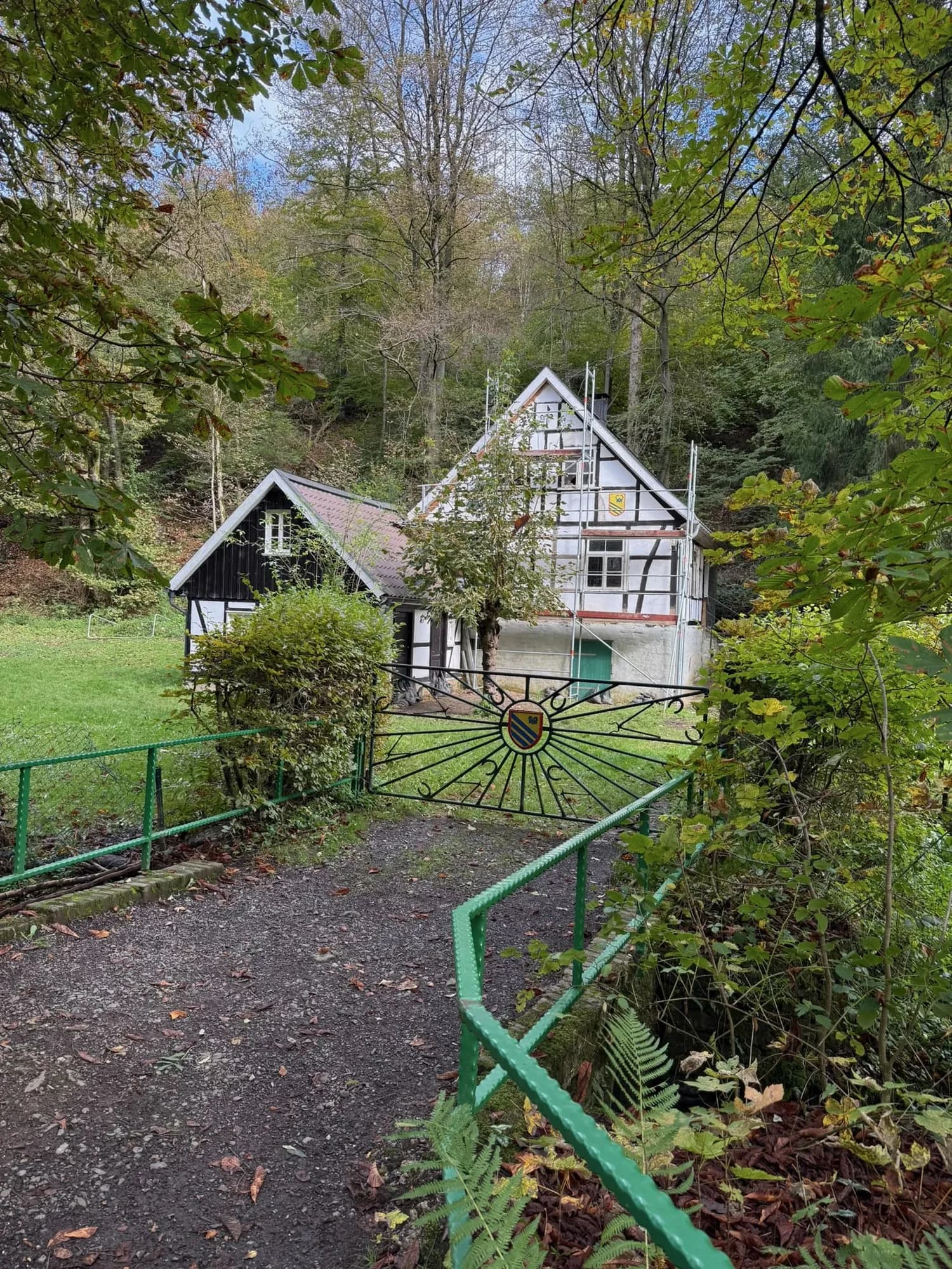 Blick über das grüne Tor auf den Kotten im Herbstlaub, das Wohnhaus mit Fachwerkgiebel ist noch eingerüstet.