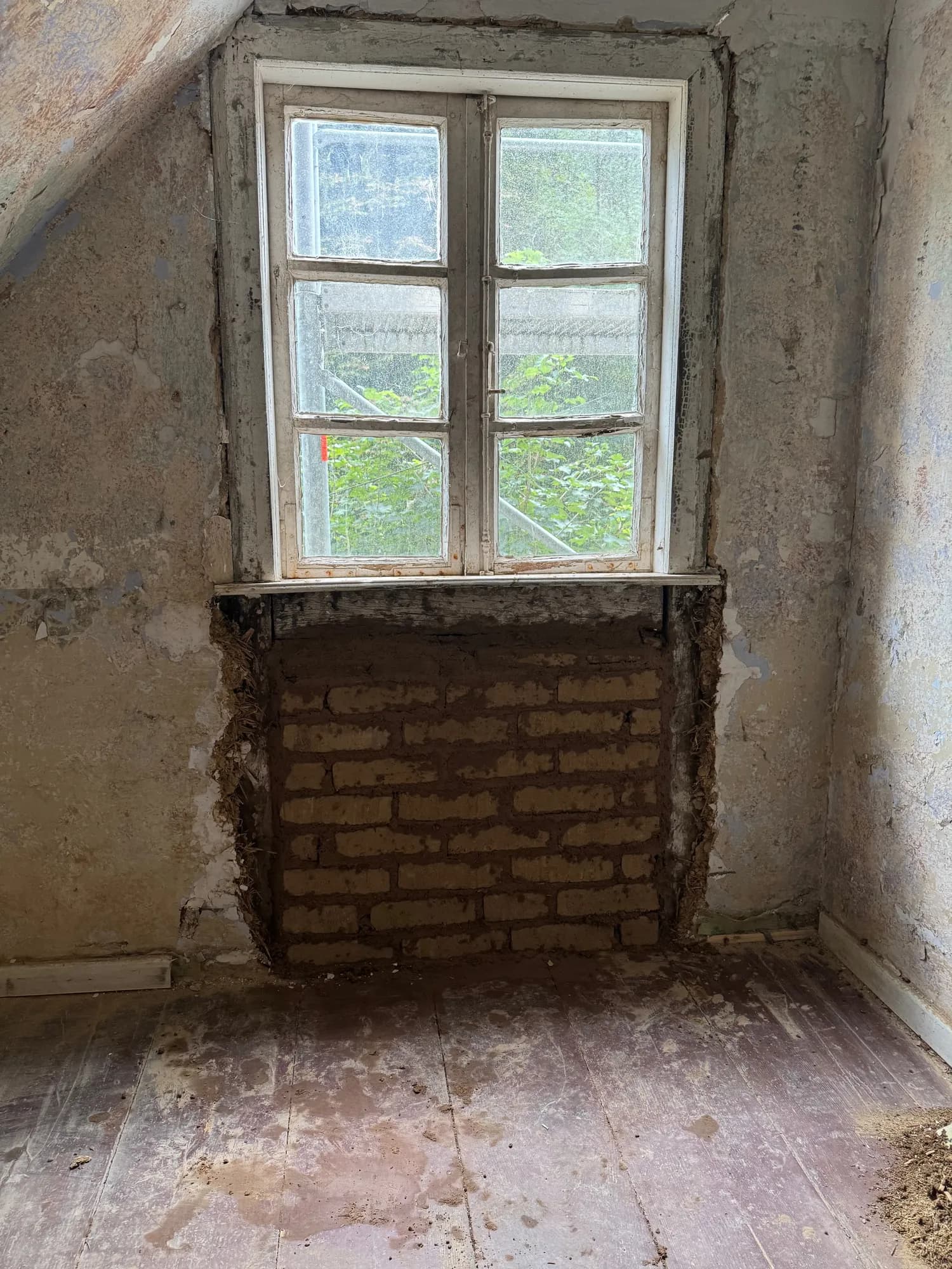 Dachgeschossraum mit Sprossenfenster, darunter eine frisch aus Lehmsteinen gemauerte Brüstung.