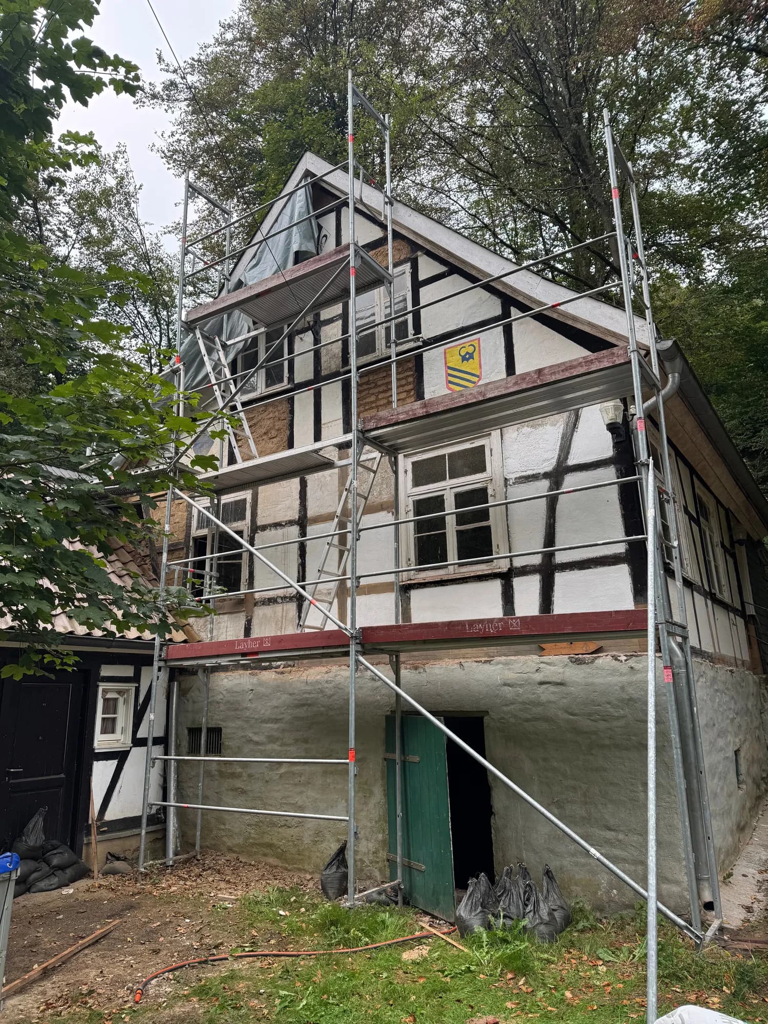 Fachwerkgiebel mit Gerüst und Plane, die Gefache teils weiß verputzt, teils mit freiliegendem Lehm oder Ziegel.
