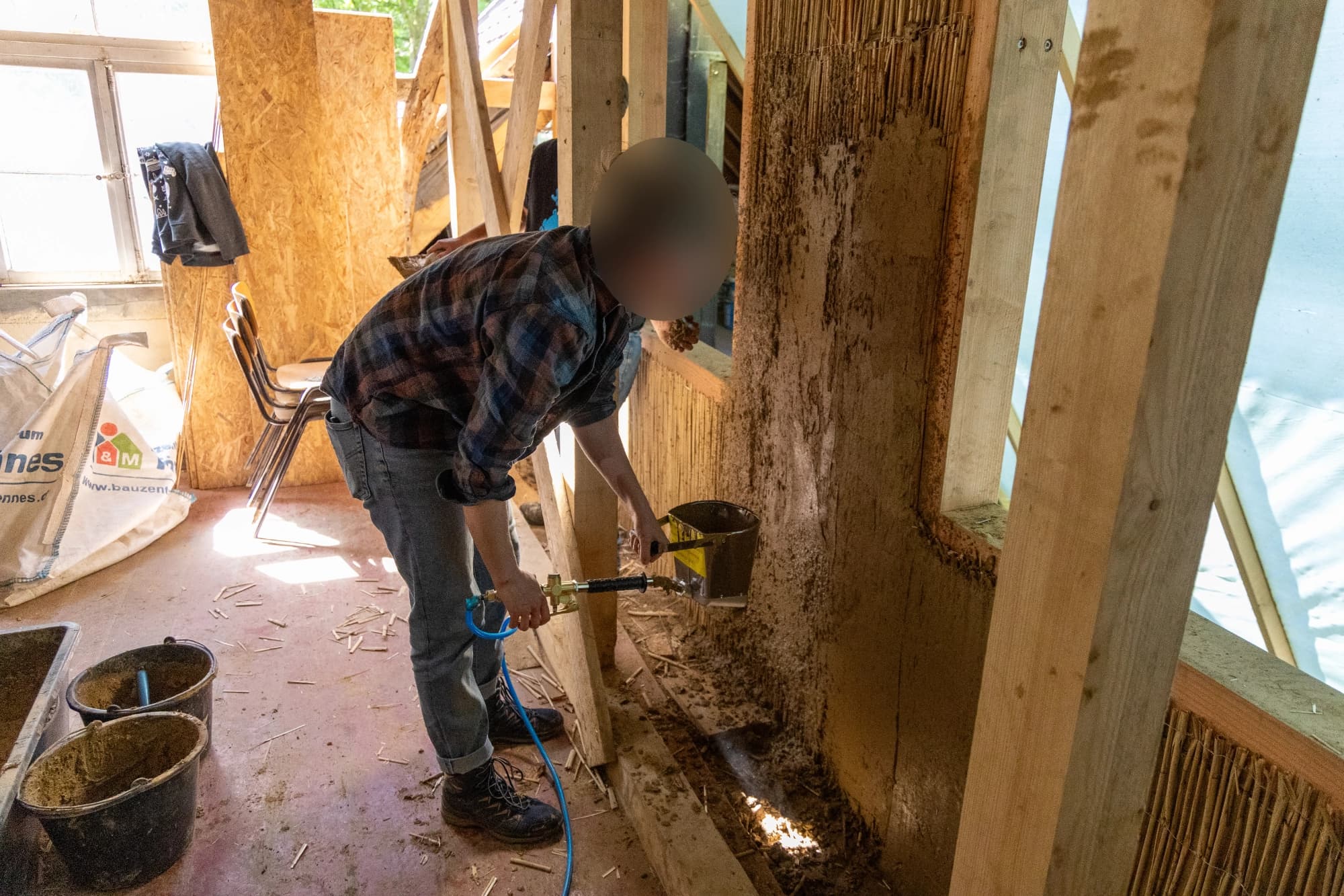 Lehmputz wird mit Druck auf die Wände gespritzt.